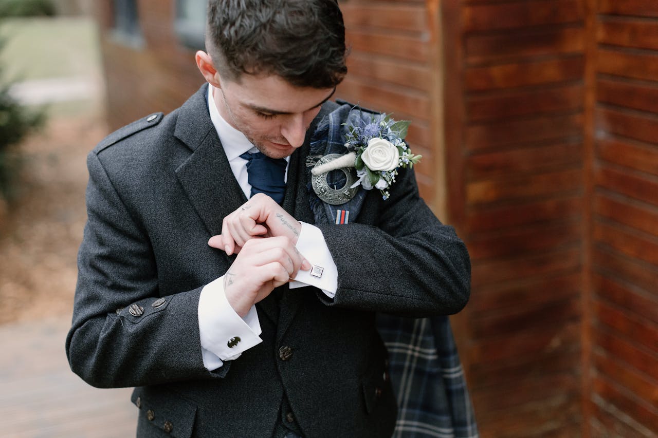 A groom in a suit adjusting cufflinks with a boutonniere on an elegant wedding day.