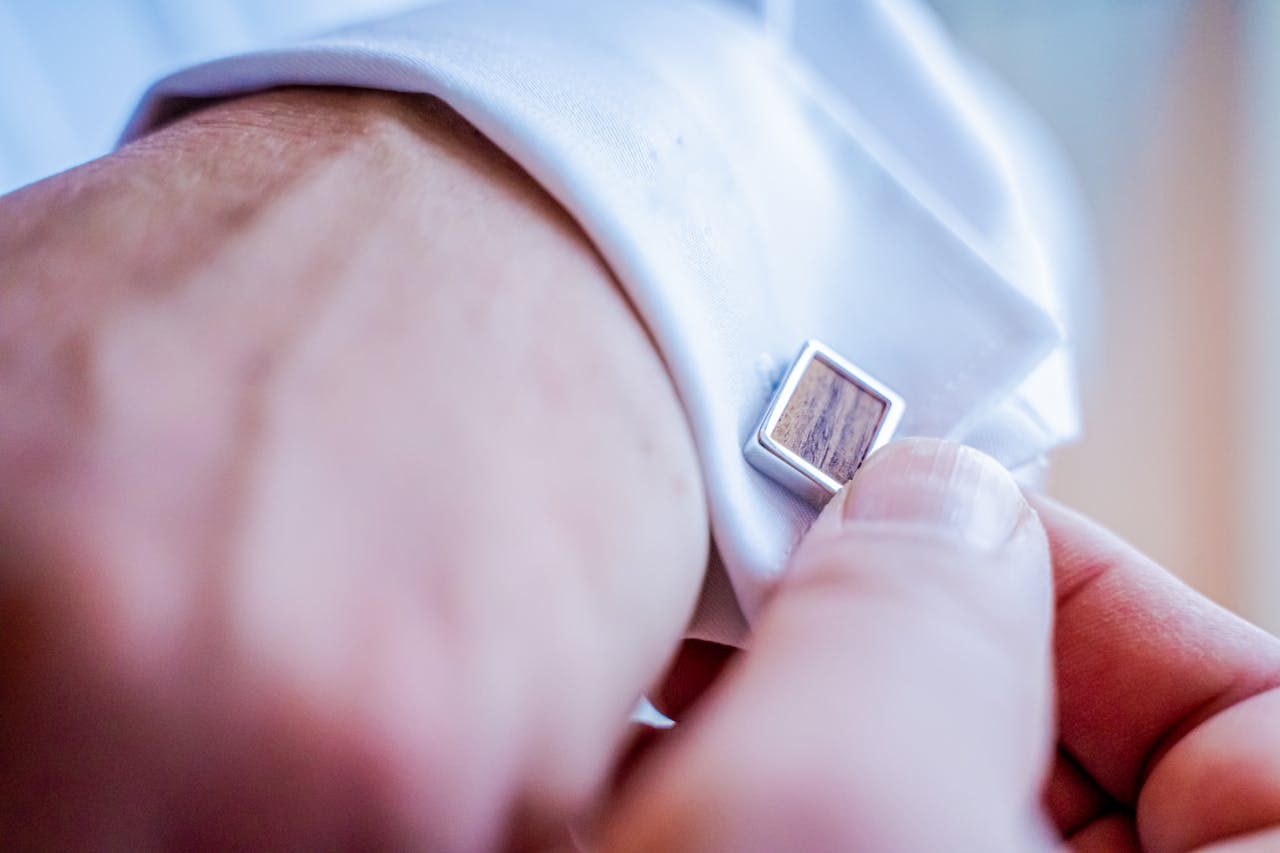 Close-up of a man adjusting his cufflinks on a white dress shirt, showcasing elegance and style.