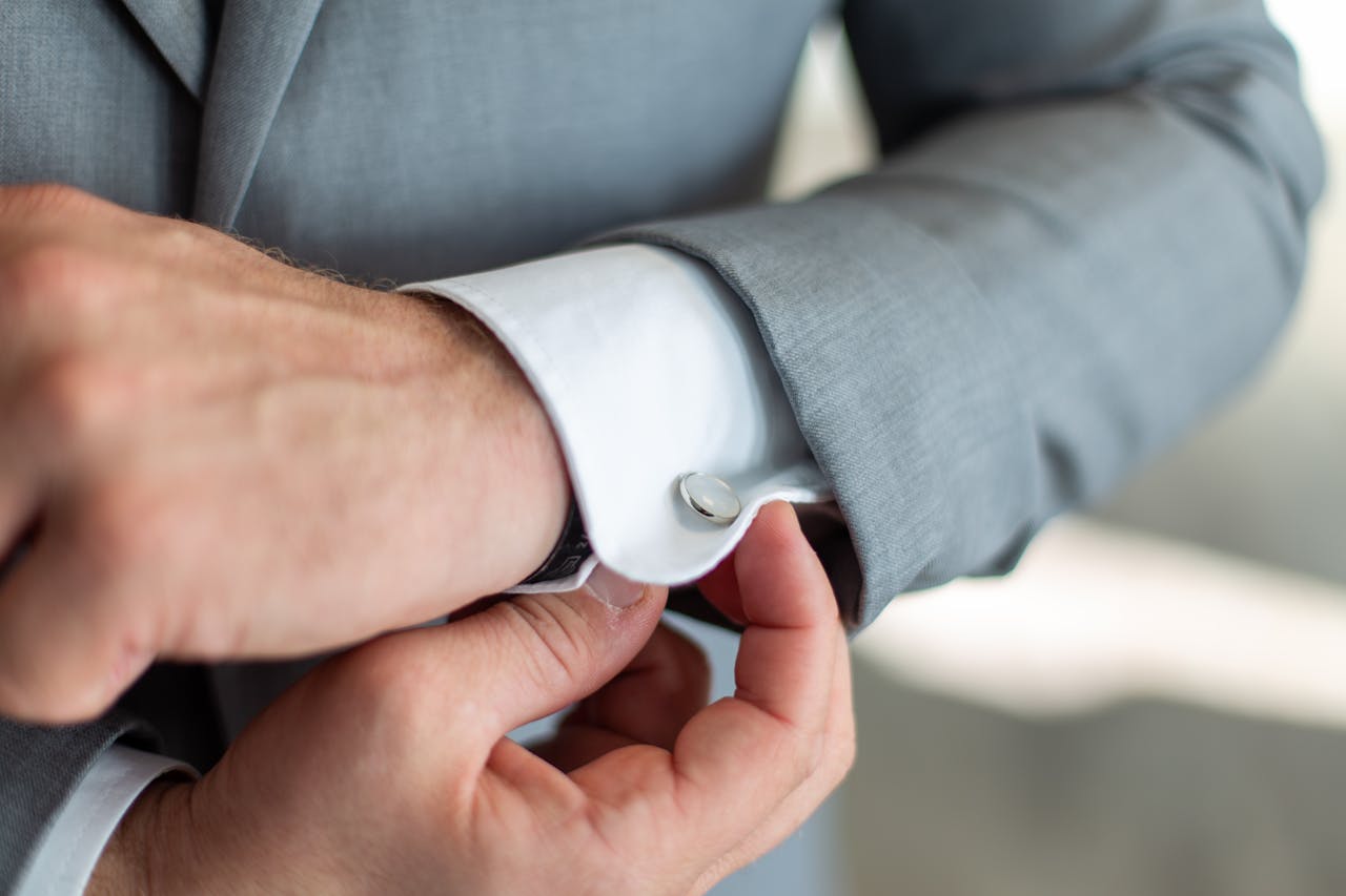 Close-up of a man's hands adjusting his cufflinks on a gray suit sleeve, showcasing elegance.